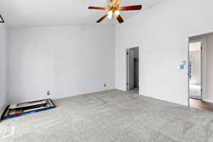Unfurnished bedroom featuring light carpet, a walk in closet, vaulted ceiling, and a ceiling fan