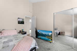 Carpeted bedroom featuring a high ceiling and a closet