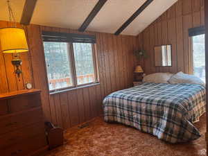 Bedroom featuring wood walls, dark carpet, and beamed ceiling