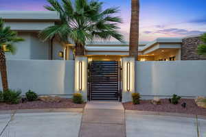Exterior entry at dusk featuring a gate and stucco siding
