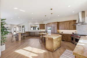 Kitchen featuring premium appliances, wood finish cabinetry, light stone counters, and light wood finished floors