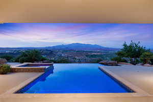Pool at dusk featuring a mountain view and a pool with connected hot tub