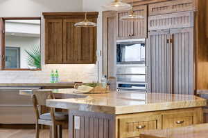 Kitchen with light stone counters, stainless steel appliances, tasteful backsplash, light wood finished floors, and decorative light fixtures