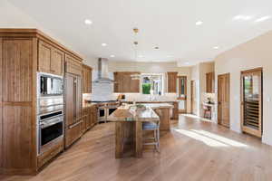 Kitchen featuring a center island, wood finish cabinets, light wood-type flooring, a breakfast bar, and premium appliances