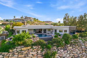 Back of house featuring stucco siding, a patio, a pool with connected hot tub, and stone siding
