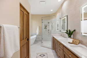 Bathroom with double vanity, a freestanding bath, light tile patterned flooring, a shower stall, and tile walls
