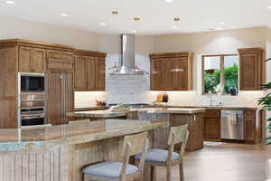Kitchen featuring wood finish cabinets, built in appliances, extractor fan, light stone countertops, and decorative light fixtures