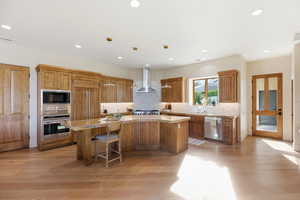 Kitchen featuring wood finish cabinetry, light wood finished floors, stainless steel appliances, a kitchen island, and hanging light fixtures