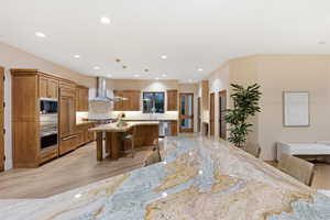Kitchen featuring a breakfast bar area, a center island, wood finish cabinetry, pendant lighting, and light stone counters