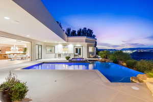Pool at dusk featuring a patio, a pool with connected hot tub, and an outdoor kitchen
