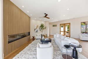 Living area featuring light wood-type flooring, recessed lighting, a glass covered fireplace, ceiling fan, and french doors