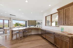 Kitchen featuring open floor plan, light stone counters, light wood finished floors, decorative backsplash, and a peninsula