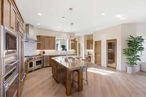 Kitchen with a kitchen island, wood finish cabinetry, stainless steel appliances, light wood-style floors, and pendant lighting