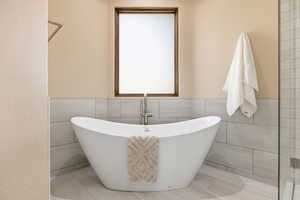 Bathroom featuring tile walls, a freestanding bath, a wainscoted wall, and light tile patterned floors