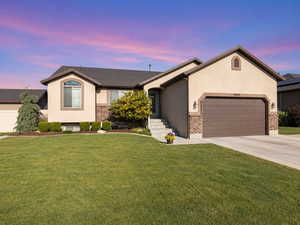 Ranch-style home featuring brick siding, a garage, a yard, concrete driveway, and stucco siding