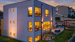 Back of house at dusk featuring stucco siding, a patio area, outdoor dining area, and stone siding