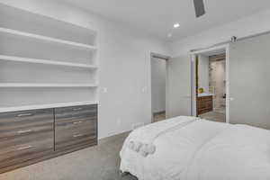 Bedroom with a barn door, recessed lighting, dark colored carpet, ceiling fan, and connected bathroom