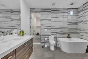 Full bathroom with tile walls, vanity, a shower stall, a soaking tub, and concrete floors