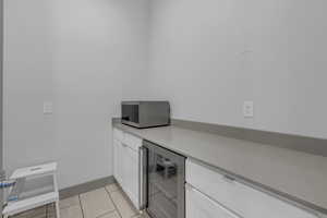 Bar area featuring beverage cooler, white cabinetry, stainless steel microwave, and light tile patterned flooring