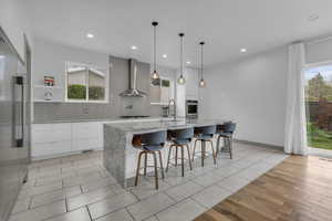Kitchen featuring light stone counters, tasteful backsplash, a kitchen breakfast bar, high quality fridge, and light wood-style floors