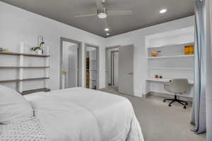 Bedroom with a walk in closet, recessed lighting, a ceiling fan, built in desk, and light carpet