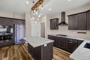 Kitchen featuring a kitchen island, stainless steel appliances, dark wood finish cabinets, and light stone countertops