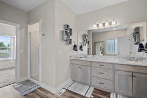 Full bath with double vanity, a shower stall, and dark wood finished floors