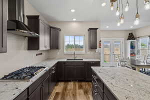 Kitchen with dark wood finish cabinets, light stone counters, stainless steel gas cooktop, and light wood-type flooring