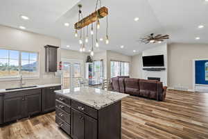 Kitchen featuring a center island, dark wood finish cabinets, light wood-style flooring, light stone counters, and lofted ceiling