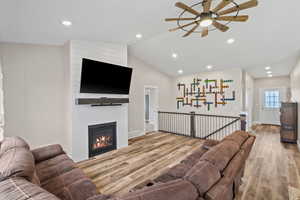 Living area featuring ceiling fan, lofted ceiling, wood finished floors, a fireplace, and recessed lighting