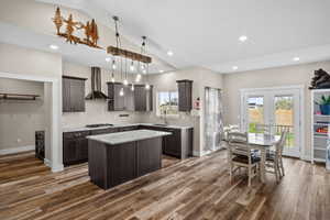 Kitchen with dark wood finish cabinets, a center island, vaulted ceiling, french doors, and light stone counters