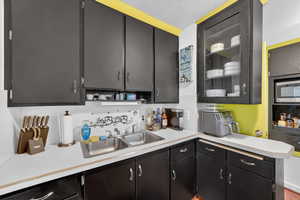 Kitchen featuring light countertops, glass fronted cabinets, a textured ceiling, and stainless steel microwave