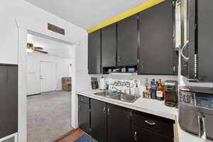 Kitchen with dark cabinetry, carpet flooring, light countertops, ceiling fan, and wood finished floors