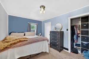 Bedroom with a closet, light carpet, and ornamental molding