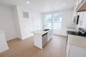 Kitchen with white cabinetry, a kitchen island with sink, stainless steel appliances, light wood-style flooring, and recessed lighting