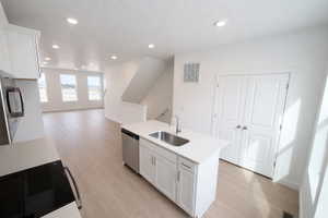 Kitchen featuring white cabinets, open floor plan, a kitchen island with sink, light wood-style flooring, and recessed lighting