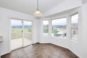 Unfurnished dining area with vaulted ceiling, plenty of natural light, and dark tile patterned floors