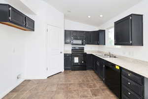 Kitchen featuring black appliances, dark cabinetry, vaulted ceiling, and light tile patterned floors