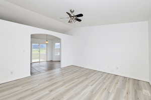 Spare room featuring a ceiling fan, arched walkways, light wood-type flooring, and lofted ceiling