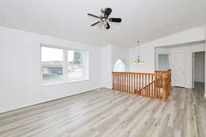 Unfurnished room featuring ceiling fan, light wood-style floors, vaulted ceiling, and a chandelier