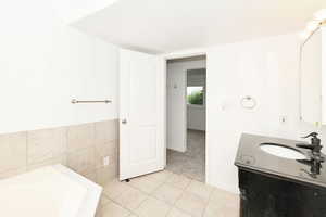 Bathroom featuring vanity, a garden tub, light tile patterned flooring, light carpet, and tile walls