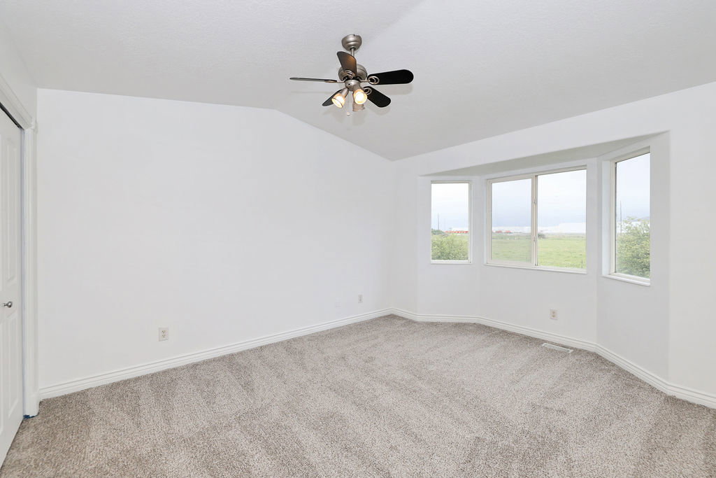 Empty room with light carpet, ceiling fan, and vaulted ceiling