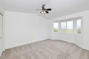 Empty room with light carpet, ceiling fan, and vaulted ceiling