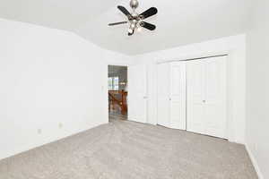 Unfurnished bedroom featuring light colored carpet, a closet, vaulted ceiling, and a ceiling fan