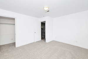Unfurnished bedroom featuring light colored carpet, heating unit, and a closet