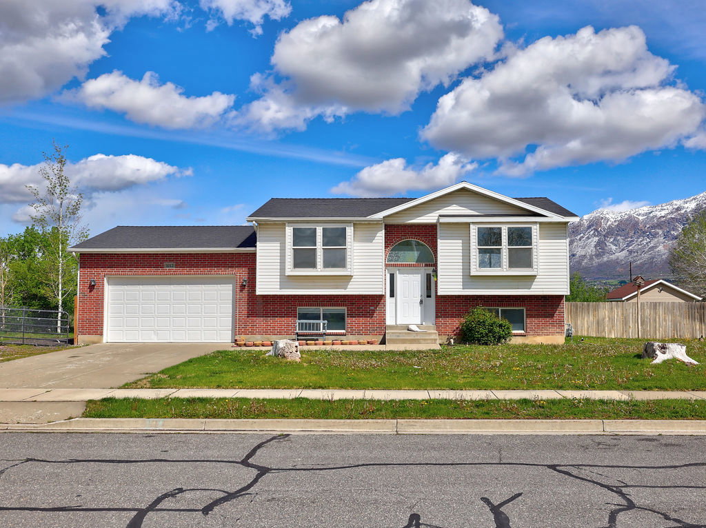 Bi-level home with an attached garage, driveway, brick siding, and a mountain view