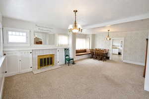 Living room with wallpapered walls, light colored carpet, a tiled fireplace, a textured ceiling, and a chandelier