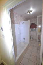 Full bath with light tile patterned floors, wallpapered walls, and shower / tub combination
