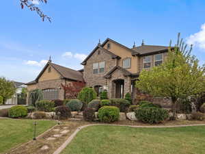 View of front of house with stucco siding, stone siding, a front lawn, and a garage