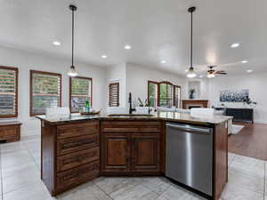 Kitchen with dark wood finish cabinetry, an island with sink, dishwasher, open floor plan, and light tile patterned flooring